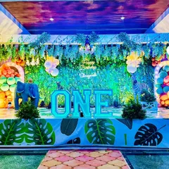 A grand safari stage decoration for a first birthday. This setup uses blue-toned lighting to create a unique nighttime jungle effect, complete with animal props and lush green decor.