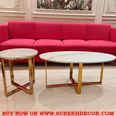 A bright and inviting living room scene featuring a bold pink four seater sofa. The space is grounded by a set of classic nesting center tables with white marble tops and a polished gold finish steel frame.