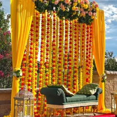A classic Haldi ceremony setup, featuring a backdrop of traditional marigold flower strings. We paired the vibrant yellow drapes with a contrasting green diwan and a lush floral arrangement on top to complete this timeless and joyful look.