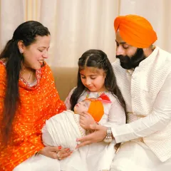 A touching moment as a family welcomes their newborn. The older sister's gentle curiosity and the parents' loving gaze are beautifully framed in their traditional Sikh attire, celebrating family and faith.