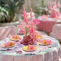 An intimate dining setup within the monochromatic pink theme. The table is set with ruffled placemats, gold-rimmed plates, and a centerpiece of pink flowers and candles wrapped in soft velvet, creating a luxurious and romantic feel.