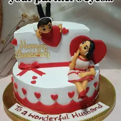A playful and romantic anniversary cake. This two-tiered design features cute fondant figurines of a couple, surrounded by hearts.