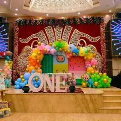 A grand stage setup for a Cocomelon first birthday party. This design uses a large 'ONE' prop, a vibrant balloon arch, and character cutouts on a fully decorated stage.