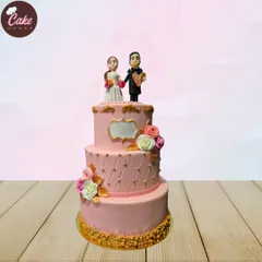 An elegant three-tiered wedding cake in a soft pink hue. It's decorated with a quilted pattern, delicate sugar flowers, and topped with a custom bride and groom figurine.