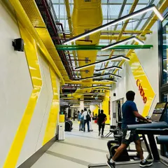 The cardio zone at the 8000 sq ft DLF Thrive Gym. An exposed ceiling with bright yellow ductwork and angular light fixtures creates an industrial yet energetic vibe, driving movement and performance.