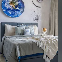 A wider view of the space-themed bedroom, showing the layered bedding in calming blues and creams that keeps the room cozy and inviting for a little explorer.