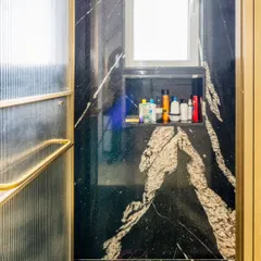 The shower area is clad in breathtaking black granite with bold white veins. The built-in niche provides practical storage for toiletries, keeping the space sleek and organized.