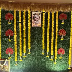 A Krishna-themed backdrop on a greenery wall. The design features hanging marigold garlands, lotus cutouts, and a central image of baby Krishna, ideal for naming ceremonies or Janmashtami.