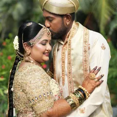 A tender moment between the bride and groom. He wears a traditional cream colored kurta with delicate gold embroidery on the stole, perfectly matching the tones of her embellished bridal saree.
