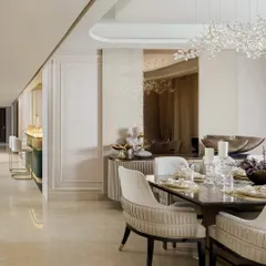 A dining area designed for graceful gatherings. The space features plush, custom-upholstered chairs, a dark tabletop for contrast, and a delicate crystal chandelier that blooms overhead, creating an elegant setting for shared meals.