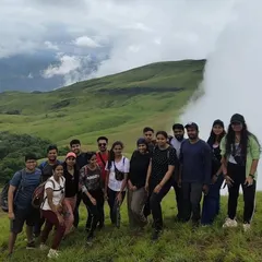 A happy group of trekkers on the rolling green hills of Netravati Peak. The clouds moving in add a touch of magic to the landscape, making for an unforgettable group experience.