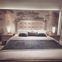 For this bedroom, we went for a classic, timeless feel. The centerpiece is a tufted, winged headboard, set against a beautiful monochromatic wallpaper depicting a forest scene. The symmetrical arrangement of the bedside tables and lamps creates a sense of perfect balance and tranquility.