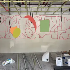 The very beginning of the 42-foot office mural. The initial red line drawings and color blocks on the raw wall show the transition from a blank space to a canvas of controlled chaos and creativity.