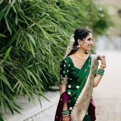 A beautiful candid portrait of the bride in her stunning green Paithani saree. Her joyful, natural smile is captured against a backdrop of vibrant bamboo, highlighting the elegance of the traditional Maharashtrian bridal look.