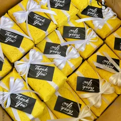 A box full of cheerful "Thank You" gifts. Each one is wrapped in bright yellow textured paper, tied with a crisp white ribbon, and finished with a bold black and white thank you tag.