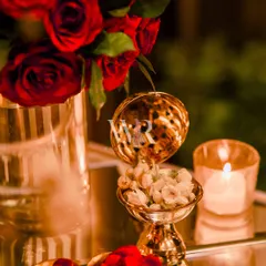 A small, ornate brass bowl filled with fragrant mogra buds sits beside a red rose arrangement. These traditional details add a layer of sensory richness and cultural depth to the decor.