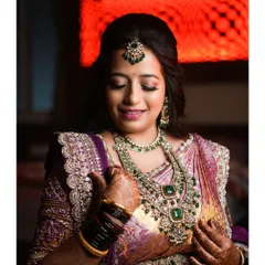A beautiful portrait of a bride in a purple saree, admiring her stunning emerald and diamond necklace.