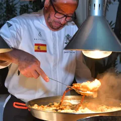 I am here preparing a large pan of paella over an open flame. This dish requires constant attention and care to ensure the rice cooks perfectly and absorbs all the flavour.