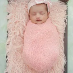 This image showcases a full view of the prop bed setup on a soft white rug. The consistent color palette with the pink swaddle and headband creates a harmonious and professional newborn photograph.