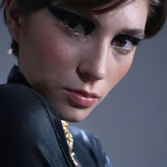 A close-up on a dramatic, thick black winged liner with a touch of gold glitter underneath for a bit of sparkle. This look combines classic glamour with a modern, edgy twist.
