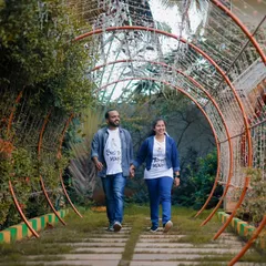 A casual walk through a garden tunnel. The couple is wearing matching "Bride" and "Groom" t-shirts, a fun detail for a pre-wedding shoot.