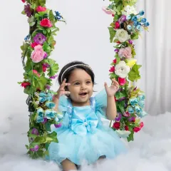 Celebrating a first birthday with a magical fairy-tale theme. This little princess is all smiles on her floral swing in the clouds.
