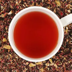 A minimalist top-down photograph of a vibrant red herbal tea, with the cup centered in a bed of its own loose leaf blend. This clean style is effective for showcasing the product's color and texture.