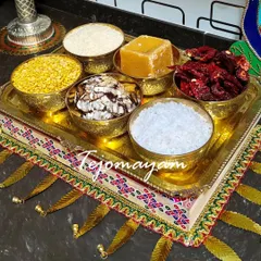 A traditional offering tray for a Gruhapravesham ceremony, featuring brass bowls filled with grains, jaggery, and other auspicious items.