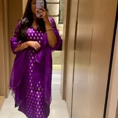 A client's mirror selfie showing off her vibrant purple brocade suit. The rich color and traditional pattern make it a standout piece for any festive occasion.