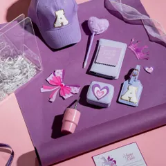 All the goodies from our purple 'Princess Treatment' hamper laid out, including a personalized cap and luggage tag, a heart-shaped lollipop, and a cute crown accessory.