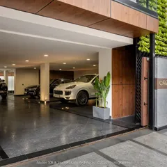 The sliding gates of the Meghana Foods office open to a sleek, functional parking area. The design uses leather-finish granite, inlaid lighting, and clean lines to create a sophisticated transitional space that houses stairways and an elevator.