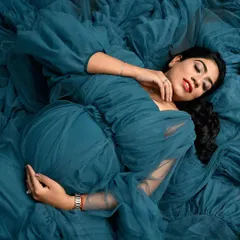 A serene and artistic top-down shot. Lying in a sea of blue tulle, this portrait focuses on the peaceful moment of connection between mother and baby.