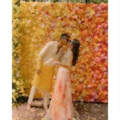 A sweet kiss against a wall of sunshine. The vibrant floral backdrop, styled with thousands of yellow and orange flowers, creates a joyful and picturesque setting for this modern haldi celebration.