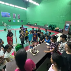 A wider view of our World Badminton Day celebration, with students gathered around the cake, ready to celebrate together at the academy.