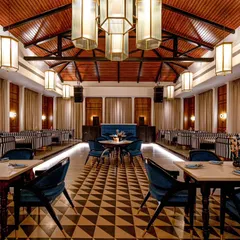 A slightly different wide perspective of Vamos Experience, this time capturing the warm, ambient lighting of the evening. The focus is on the interplay between the geometric floor, the wooden ceiling, and the soft glow from the pendant lights.