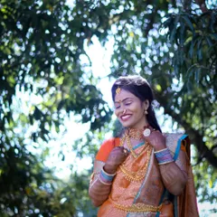 An outdoor portrait capturing a happy moment. The model is dressed in a beautiful orange saree, with the natural green background making the colors stand out.