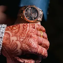 A close-up shot of the couple holding hands, highlighting the bride's mehendi and the groom's classic watch.