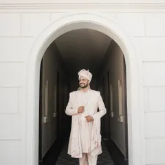 A full-length portrait of the groom in his elegant pastel sherwani, framed by a white archway, exuding calm confidence.