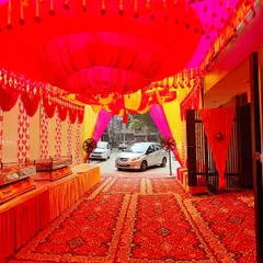 This is a tent setup in a parking area for a housewarming party. The red and yellow theme is carried from the ceiling drapes to the wall panels, and a long buffet counter is set up along the side.