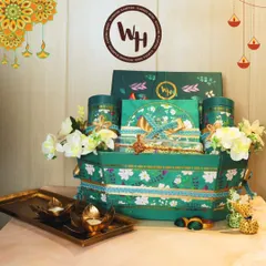 A grand festive hamper presented in a unique green floral boat-shaped basket. This arrangement is overflowing with premium teas, sweets, and decorative items, accented with white orchids and lotus-shaped diyas for a complete Diwali feel.