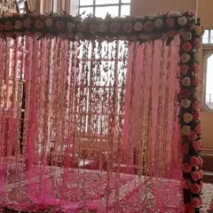 A beautiful mandap or entryway frame decorated with pink roses and a sheer pink curtain with hanging elements, creating a delicate and romantic effect.