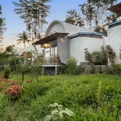 An exterior view of a Santorini-inspired villa in Coorg, with its whitewashed, curved walls nestled in a lush green landscape. The architecture offers a unique Mediterranean escape in the misty mountains.
