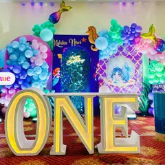 A full view of the mermaid first birthday stage, showcasing the large marquee letters, themed pedestals, and the beautiful color palette.