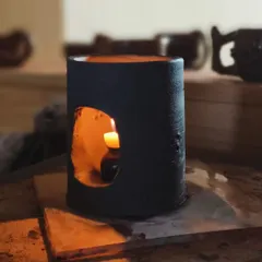 A student-made ceramic candle holder glows warmly in the studio. In our classes, you will learn to create functional pieces like this, focusing on form, cut-outs for light, and finishing techniques.