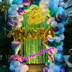 An underwater adventure with this Mermaid-themed 5th birthday. The decor features a green shimmer backdrop, a balloon arch in ocean colors, and a mermaid tail foil balloon.