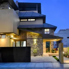 As night falls, the architectural lighting transforms the house, accentuating the texture of the stone cladding and the geometric lines of the overhangs.