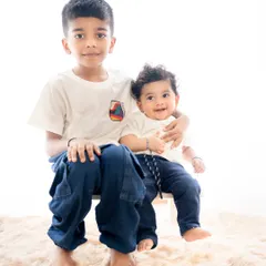 A classic portrait of an older brother proudly holding his baby brother. The clean, high-key background keeps the focus on their sweet relationship.