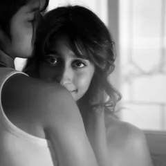 A tender black and white portrait capturing an embrace. One person looks over the other's shoulder directly at the camera, creating an intimate connection with the viewer.