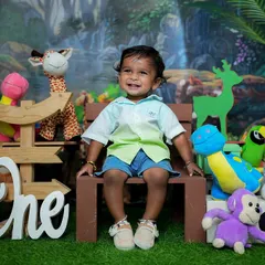 Welcome to the jungle. This first birthday shoot has a fun animal theme, with lots of plush toys, a jungle backdrop, and a happy one-year-old enjoying the setup.