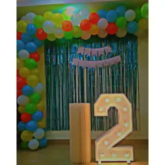 A simple and sweet decoration for a second birthday. This setup includes a multi-colored balloon arch, a shimmering tinsel backdrop, and a cute light-up number '2', making it a great option for a toddler's party.